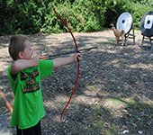 A child holding a bow and arrow at an archery range