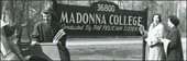 College girls surrounding a Madonna College sign in a black and white historical photo