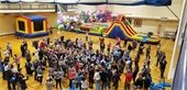 A crowd surrounded by bounce houses with falling balloons